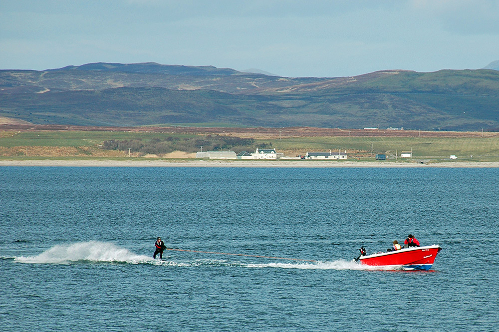 Picture of a boat pulling a water skier off a coast with an old farm
