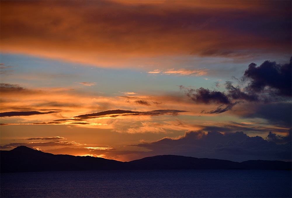 Picture of a colourful sunset behind an island seen from a passing ferry