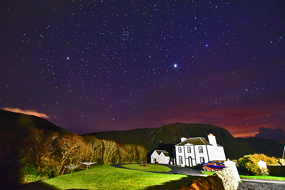 Picture of a large old house below some crags under a starry night sky