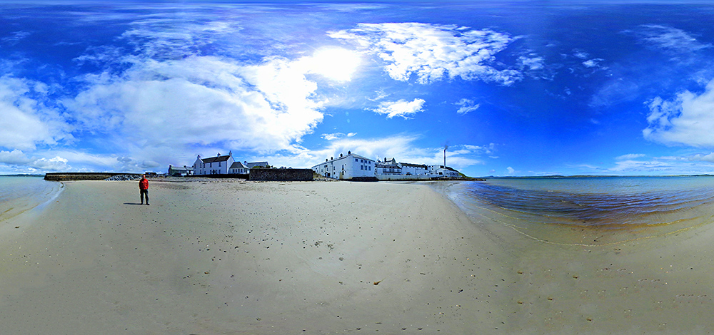 Panoramic 360° picture of a distillery seen from a beach at a sea loch