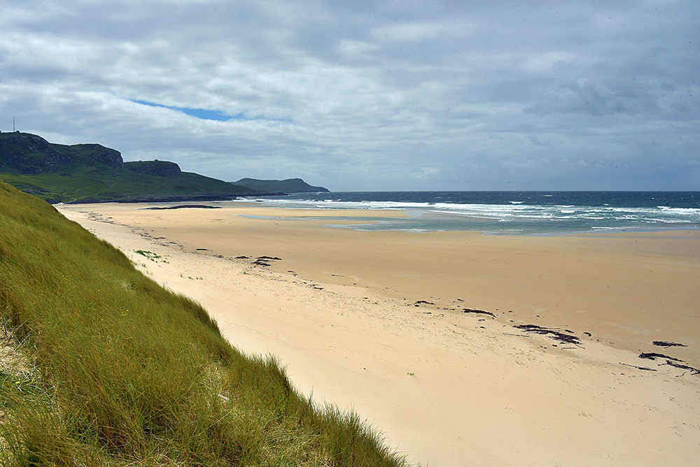 Picture of a wide beach on a cloudy day seen from some dunes