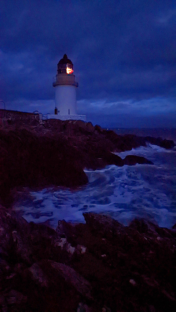 Picture of a lighthouse on a rocky shore in the last light of the gloaming