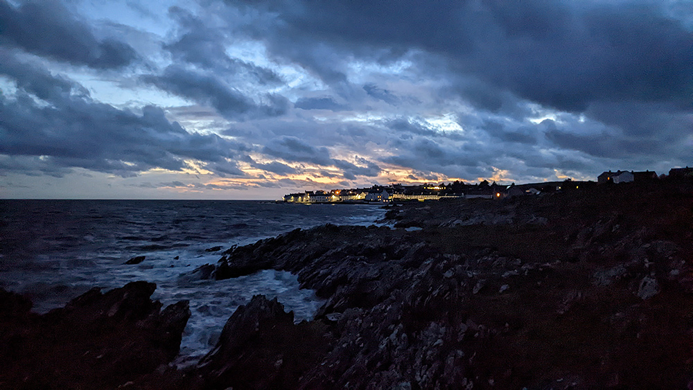 Picture of a coastal village in the last light of the gloaming, see across a rocky shore