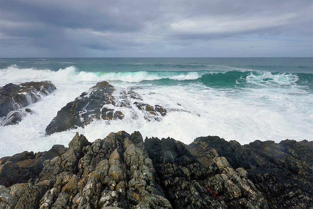 Picture of waves rolling up to and breaking over cliffs on a rocky shore