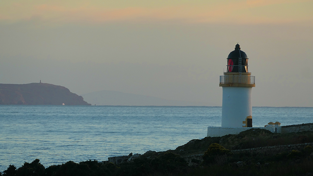 Picture of a small coastal lighthouse and a mull with a small tower at a November dusk