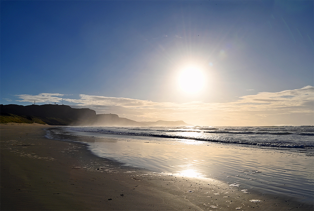 Picture of some low sun on a November afternoon over a bay with steep cliffs and a beach