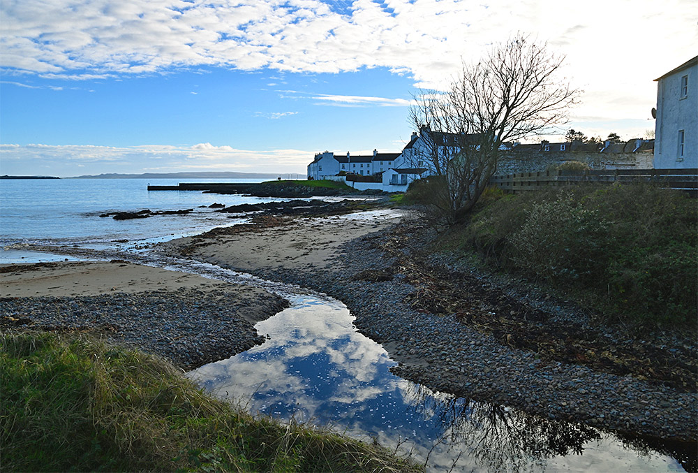 Picture of a view from a cottage garden over a small burn, a beach and a coastal village