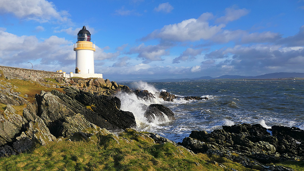 Picture of a small lighthouse on a rocky shore, waves breaking over the rocks