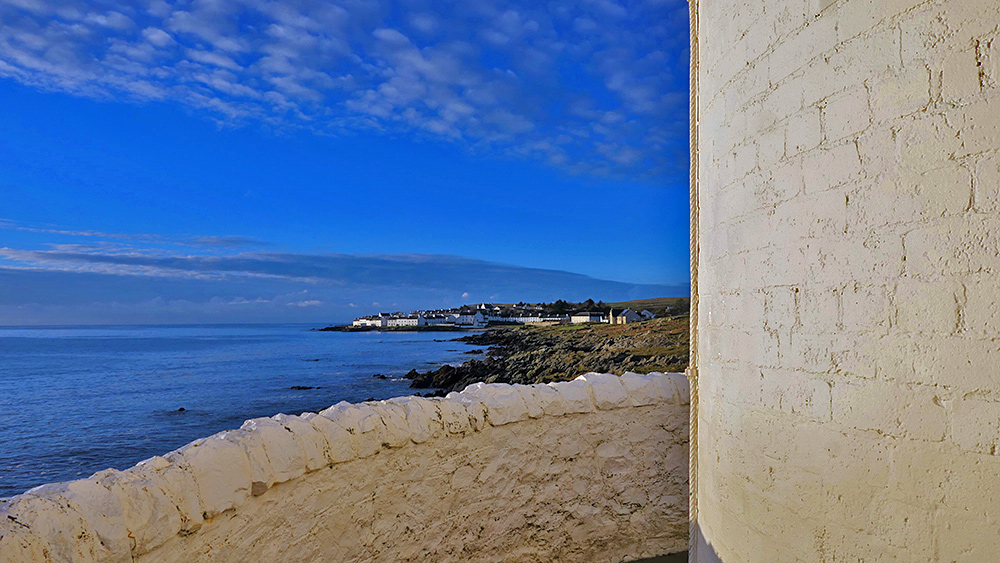Picture of a view past the wall of a whitewashed lighthouse to a coastal village
