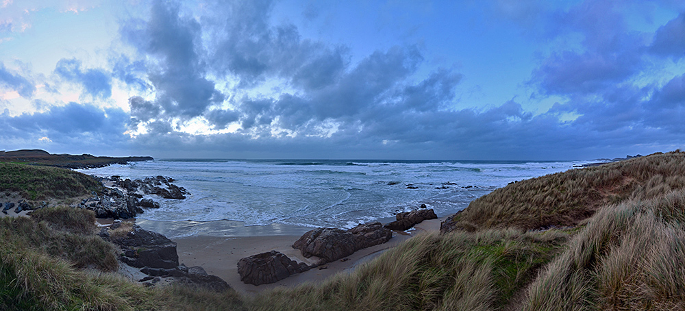 Panoramic picture of a west facing bay with a beach, dunes and rocky coastline on a November afternoon