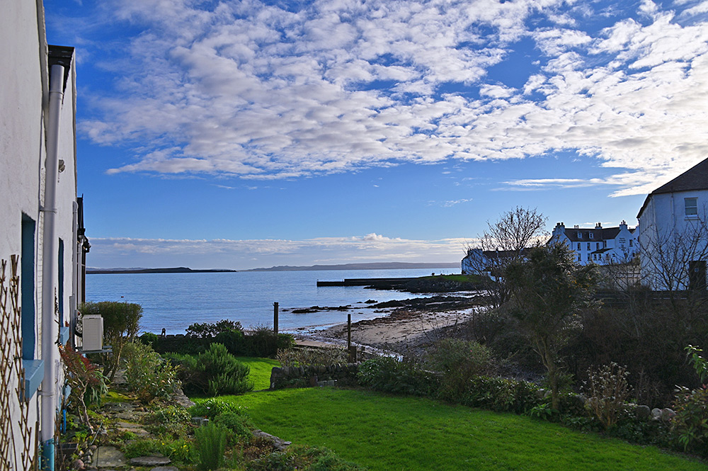 Picture of the view from the garden of a coastal cottage, looking out over a sea loch between whitewashed buildings