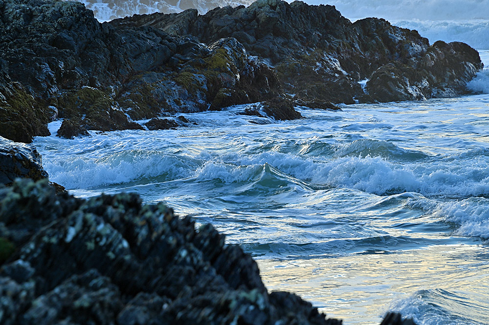 Picture of small waves breaking and swirling between rocks at the shore of a bay