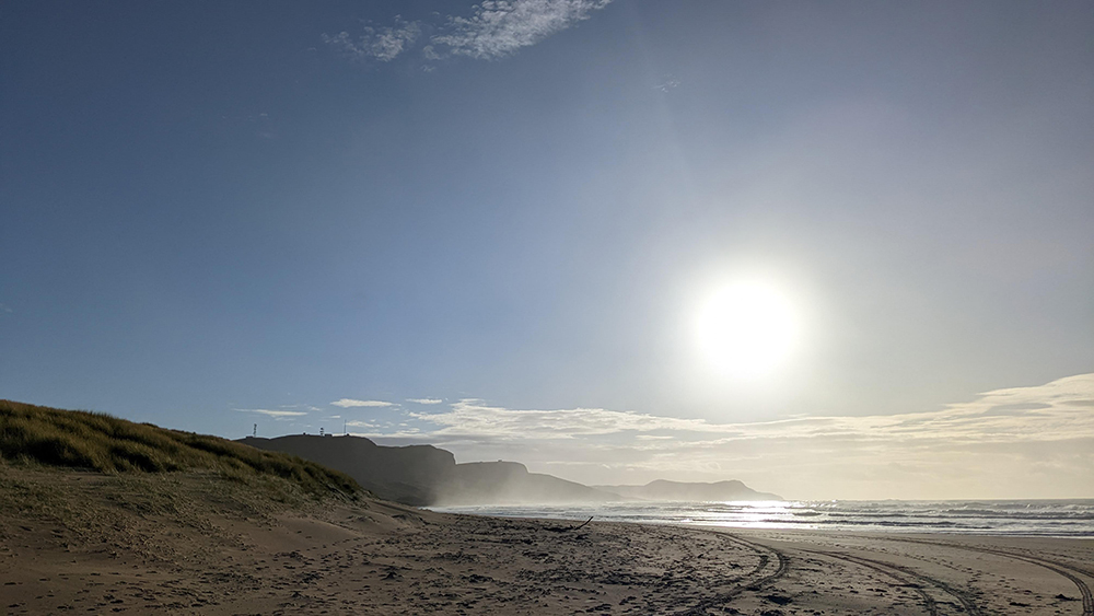 Picture of some low bright sun over a bay with a sandy beach and dunes
