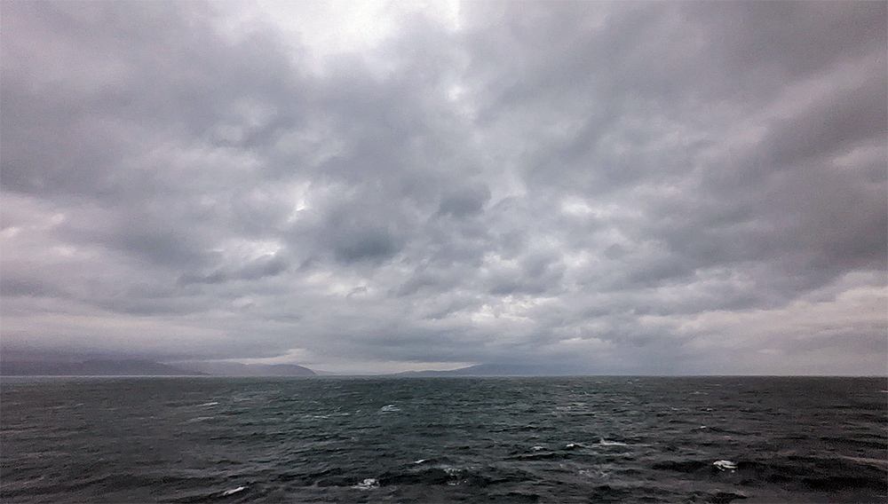 Picture of heavy clouds over a sound between two islands, seen across a dark choppy sea from a ferry
