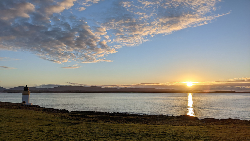 Picture of a sunrise over a sea loch, a small lighthouse at the shore