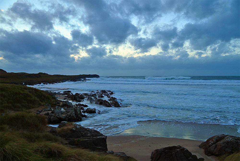 Picture of a bay on a mostly cloudy November afternoon with big waves rolling in, breaking as the approach the beach