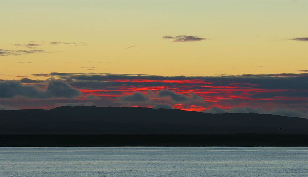 Picture of a some colourful red clouds at dawn over some hills seen across a sea loch