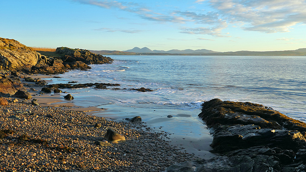 Picture of a view over a sea loch from a small beach, some mountains in the distance
