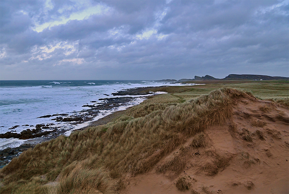 Picture of a bay with a rocky shoreline and some beach stretches as well as some dunes under some heavy November clouds
