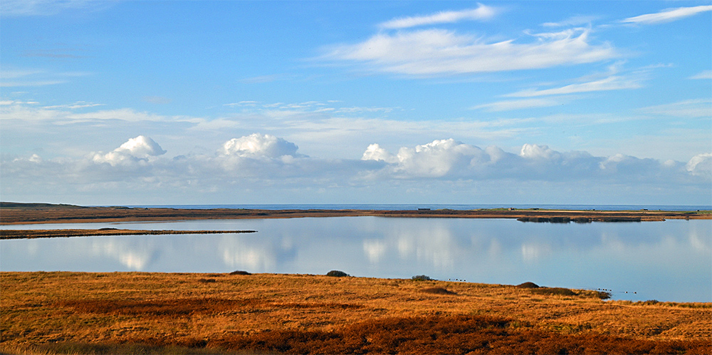 Picture of a calm freshwater loch on a November afternoon, the ocean in the background