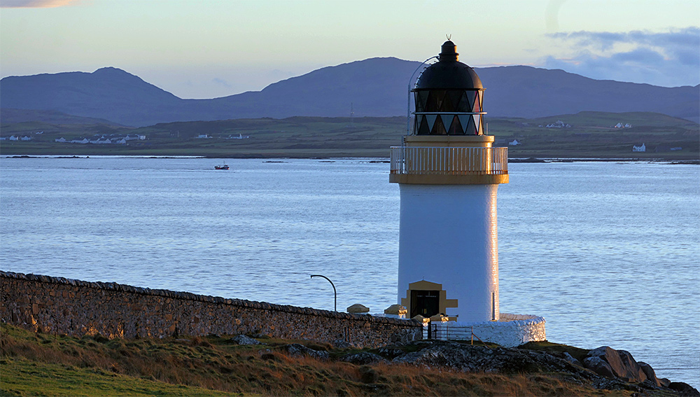 Picture of a small lighthouse at a sea loch, a passing fishing boat in the background