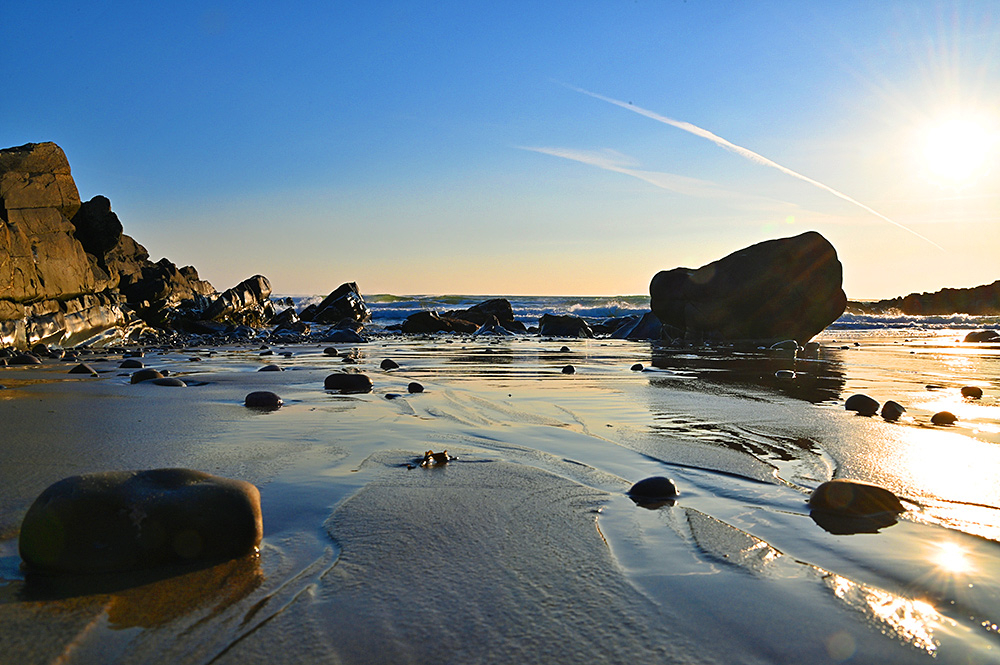 Picture of a small sandy beach with stones and boulders strewn across under some nice mild April evening light