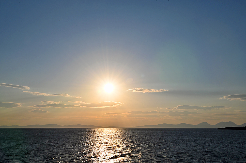 Picture of some bright evening sun over two islands in the distance, seen across the sea from a ferry