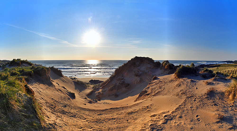 Picture of some evening sun behind some dunes above a bay