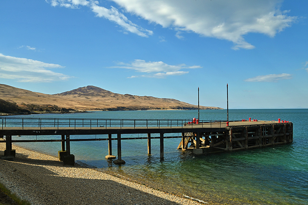Picture of a distillery pier with a coastline stretching out into the distance behind, a small hill in the centre