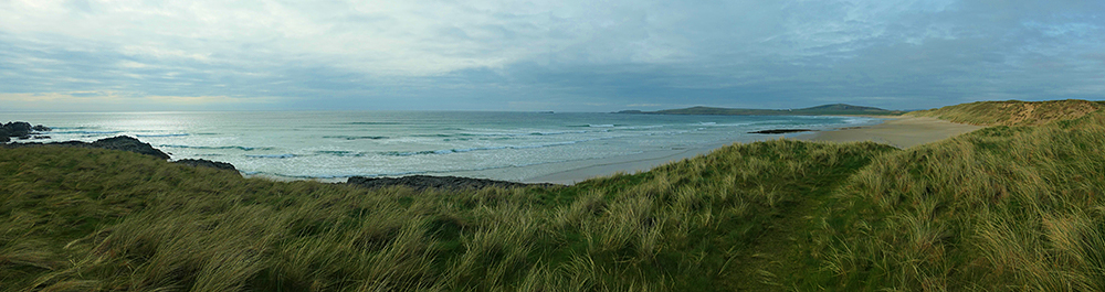 Panoramic picture of a wide bay with a beach, seen from dunes at the end of the beach