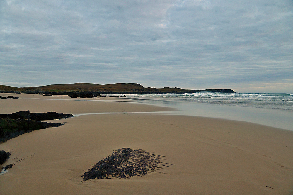 Picture of a view over a sandy beach with some rocks on an overcast evening