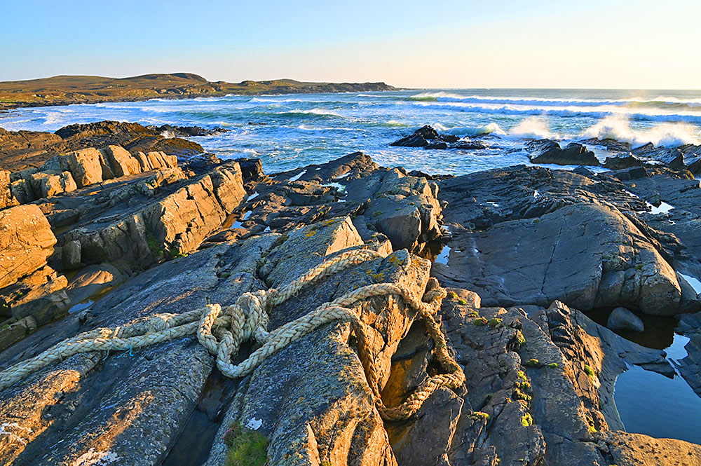 Picture of a large rope on some coastal rocks/cliffs in the mild light of an approaching sunset