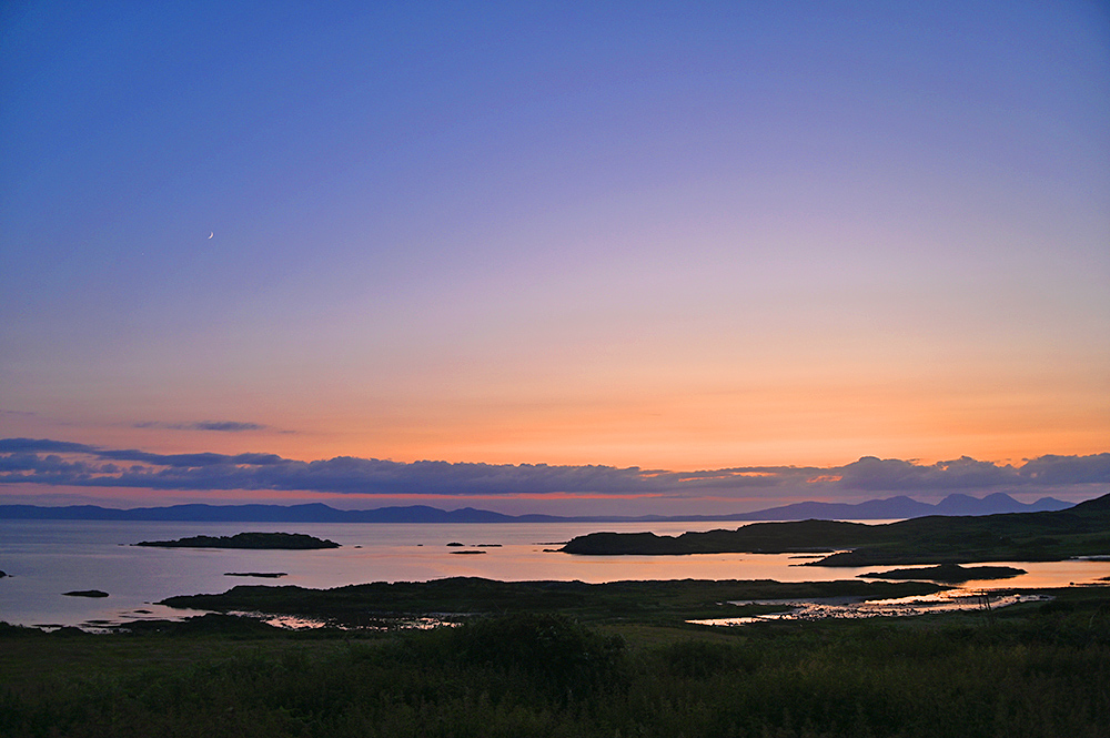 Picture of a colourful evening sky during the gloaming after sunset over a coastal landscape with a view to two distant islands