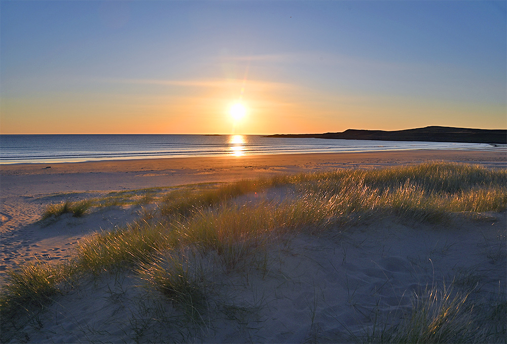 Picture of a sunset over a wide bay with a sandy beach seen from some dunes