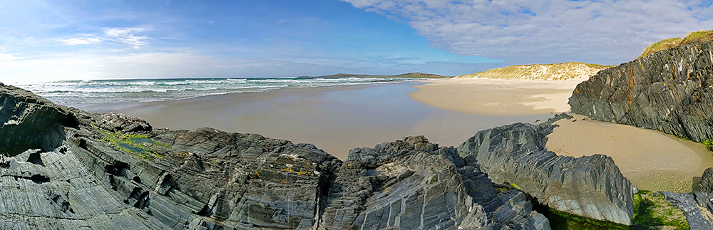 Panoramic picture of a beach with dunes at the back seen from some rocks