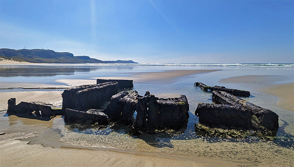 Picture of the remains of an old wreck embedded in a beach, seen on a sunny April day