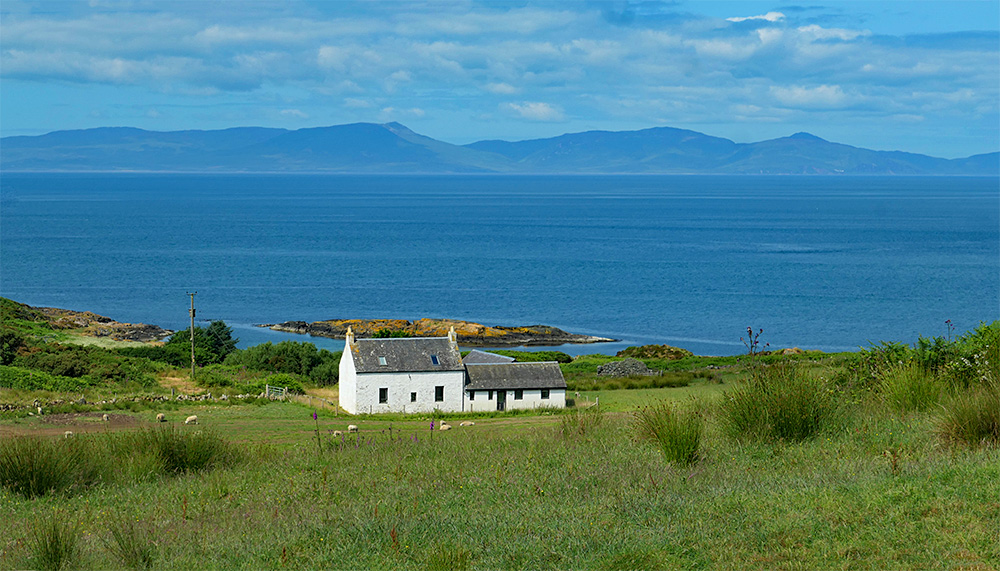 Picture of a whitewashed cottage at an island coast, another island in the background in the distance