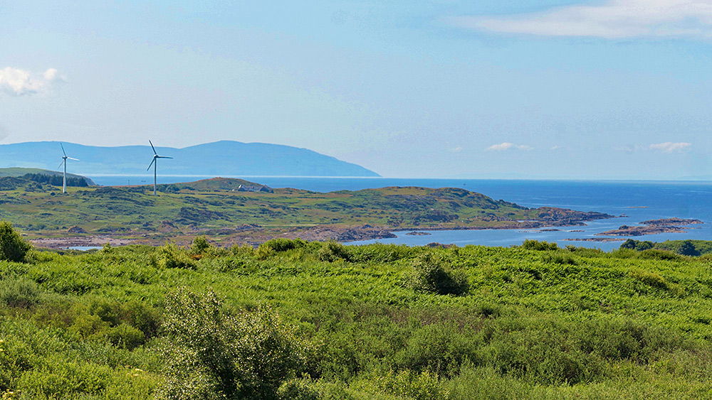 Picture of a view over the coast of an island with two wind power engines, the mainland in the distance