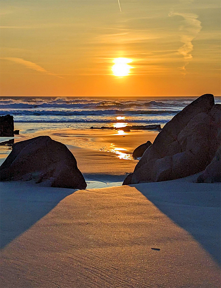 Picture of a sunset watched between some rocks on a sandy beach