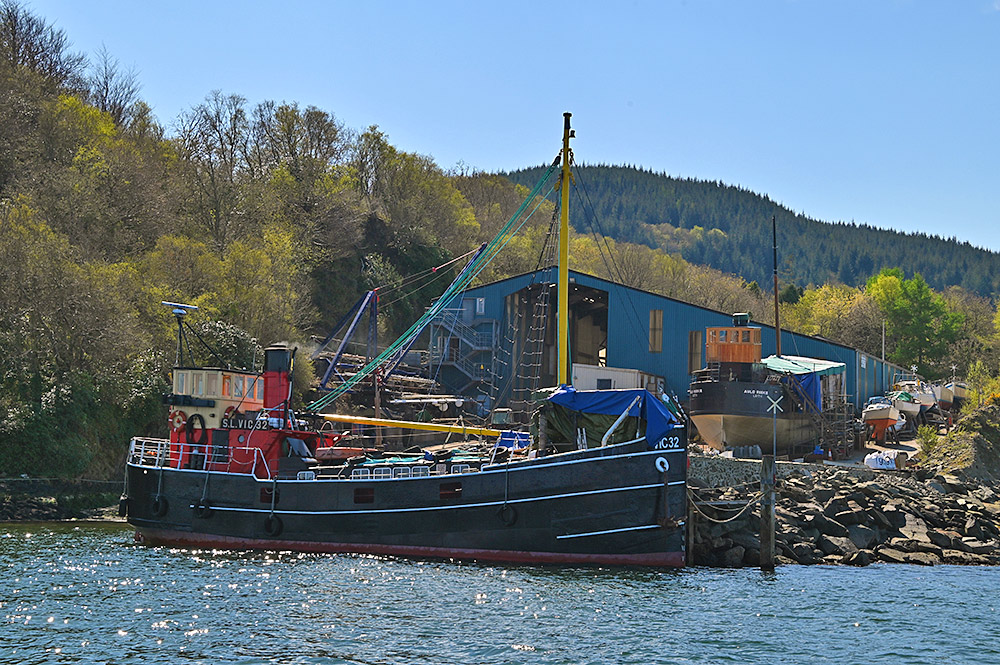 Picture of two puffer ships at a small boatyard, one in the water, the other up on land