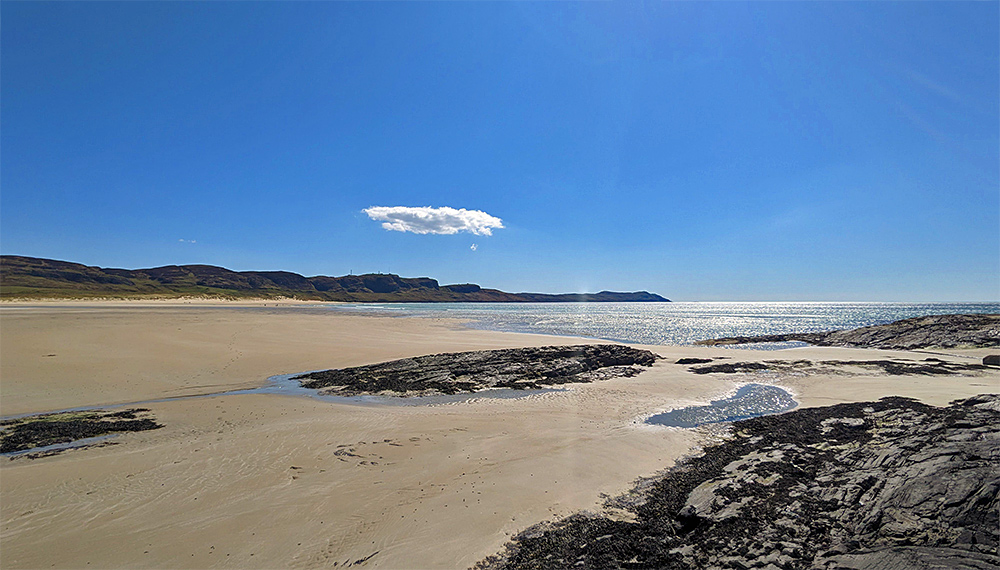 Picture of a bright sunny view over a wide sandy beach, a single lone fluffy cloud in the sky