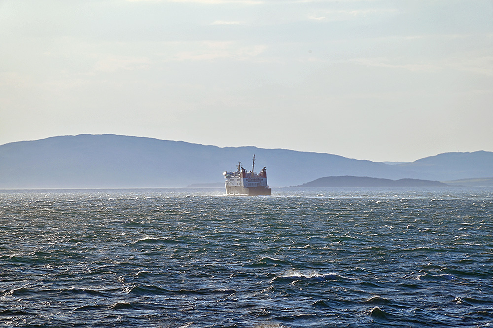 Picture of a CALMAC ferry approaching a sound between two islands in some rising mist