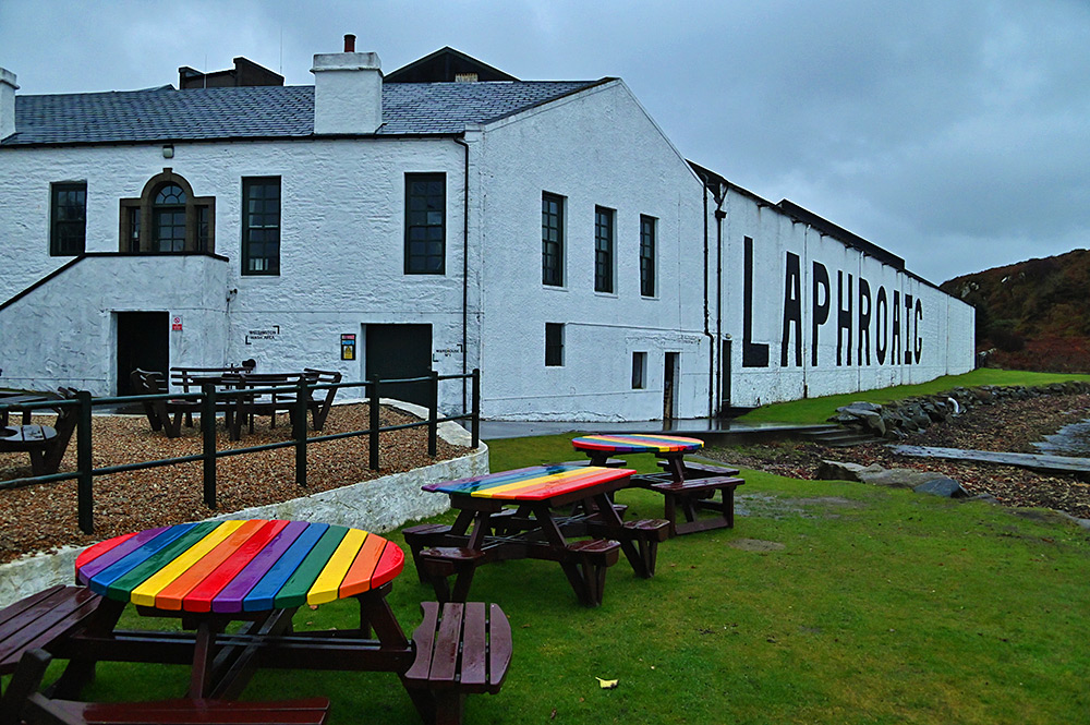 Picture of Laphroaig distillery on a cloudy and wet afternoon with colourfully painted tables outside