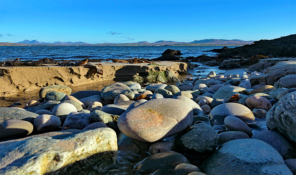 Picture of some rocks and stones in a small stream running across a beach, seen from a low angle