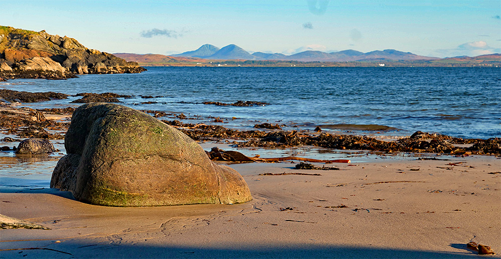 Picture of a smooth rock on a small beach at a sea loch, some mountains in the distance on the other side