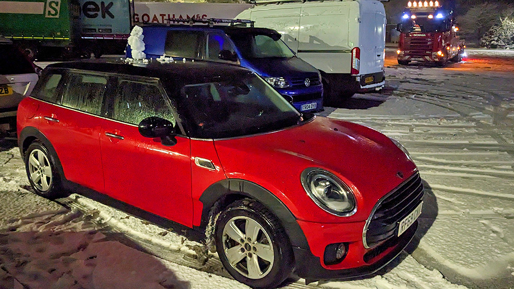 Picture of a very small snowman on top of a Mini Clubman car