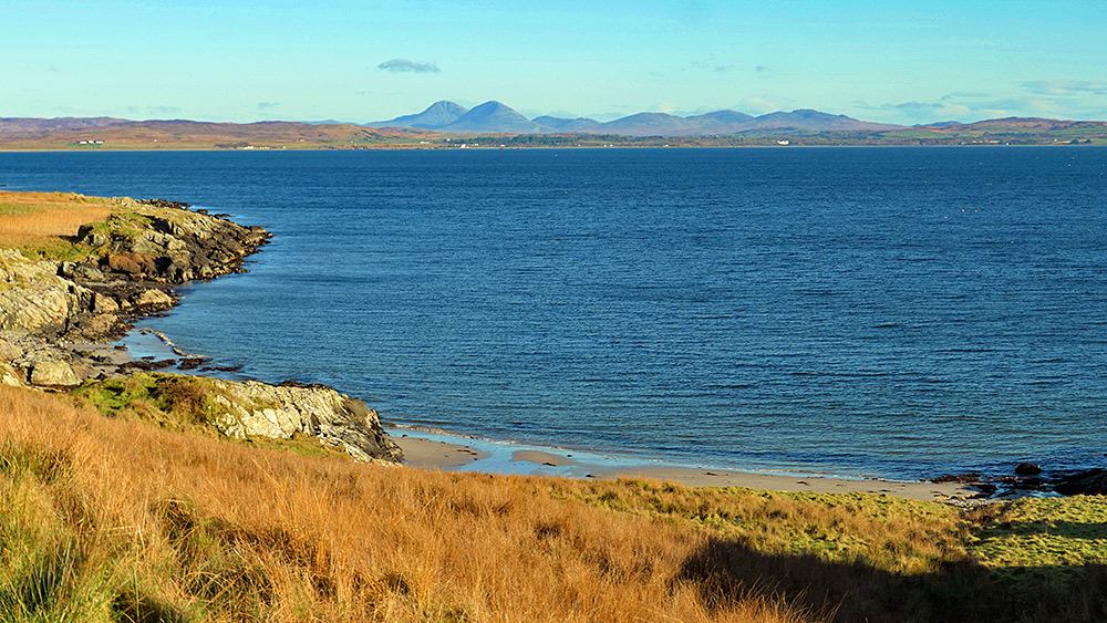 Picture of a view over a small beach at a sea loch with some mountains in the distance