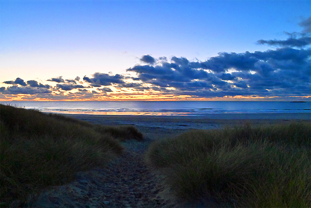 Picture of a view from a path through dunes over a beach and a bay in the gloaming after sunset