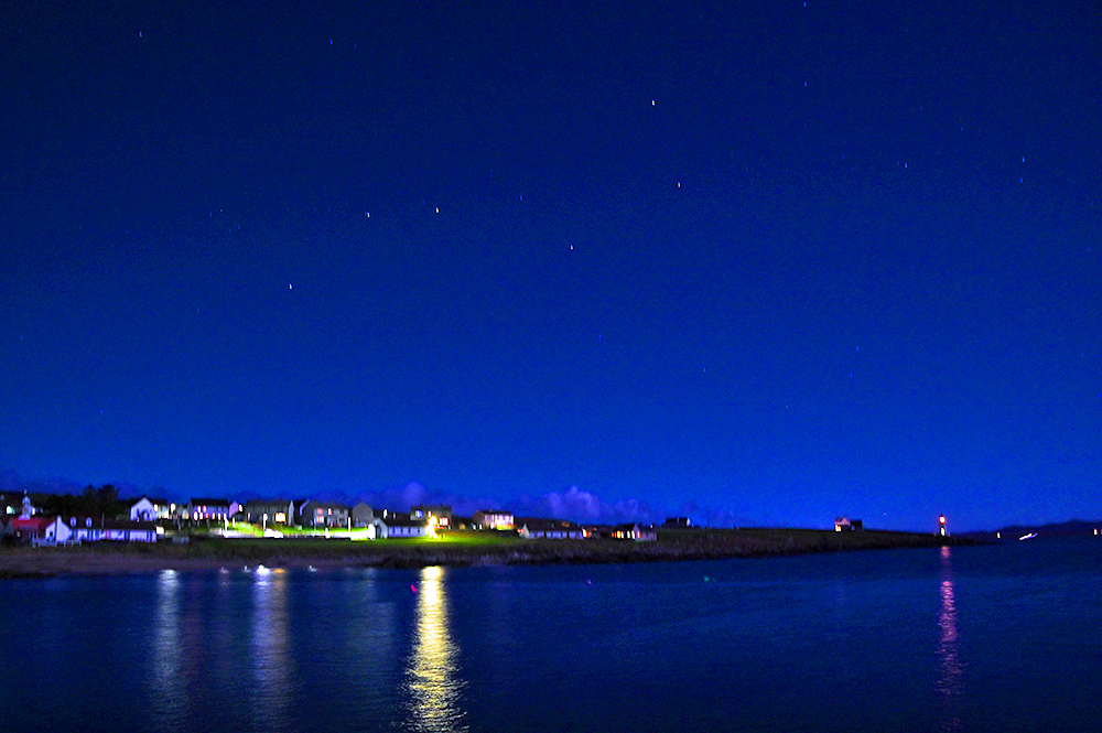 Picture of a coastal village during a moonlit night with some stars visible in the sky