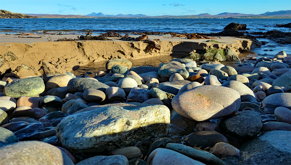 Picture of smooth rocks in a small burn running over a beach into a sea loch